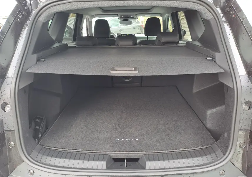 Vue arrière du coffre ouvert du Dacia Bigster noir nacré, avec cache-bagages et tapis de sol marqué Dacia.
