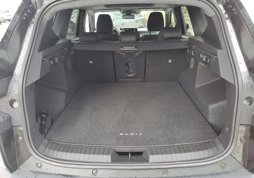Coffre ouvert vu de l'arrière d'un Dacia Bigster noir nacré, avec tapis de sol marqué Dacia et banquette arrière visible.