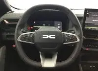 Gros plan sur l’inscription Bigster sur la carrosserie noir nacré d’un Dacia Bigster, reflet de voitures en arrière-plan.