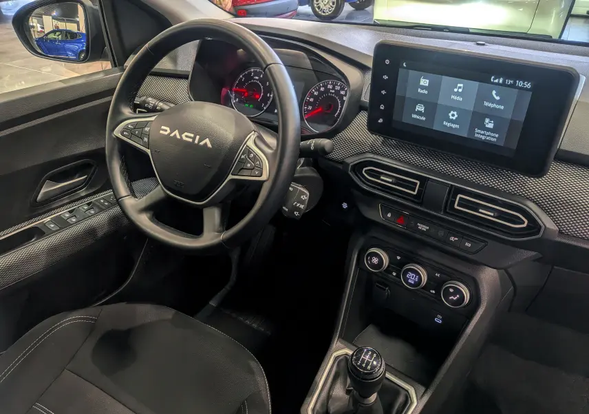 Vue intérieure côté conducteur du tableau de bord et volant DACIA Sandero TCe 90 gris, avec écran tactile et levier de vitesse manuel.
