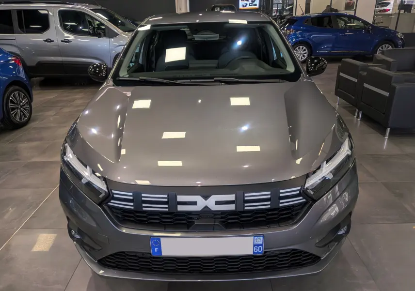 Vue de face d'une Dacia Sandero TCe 90 gris schiste, avec calandre noire et phares LED, en showroom intérieur.