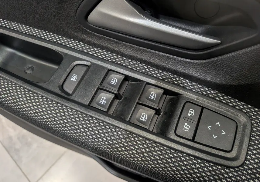 Gros plan sur les commandes des vitres électriques et rétroviseurs sur la portière côté gauche de la Dacia Sandero TCe 90 Gris Schiste 2025.