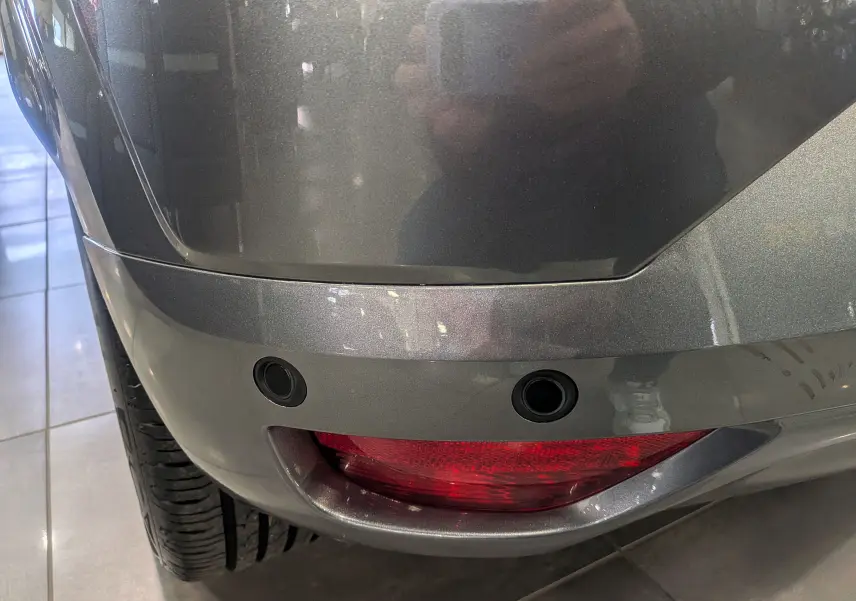 Gros plan sur le pare-chocs arrière gris schiste d'une Dacia Sandero 2025, avec capteurs de recul et feu antibrouillard.