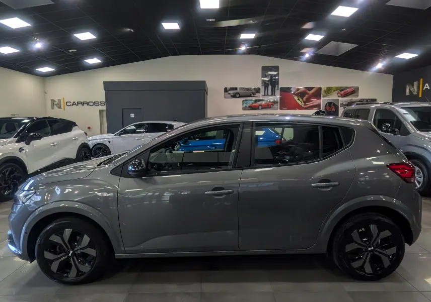 Vue de profil côté gauche d'une Dacia Sandero TCe 90 gris schiste, avec jantes alliage noires en showroom.