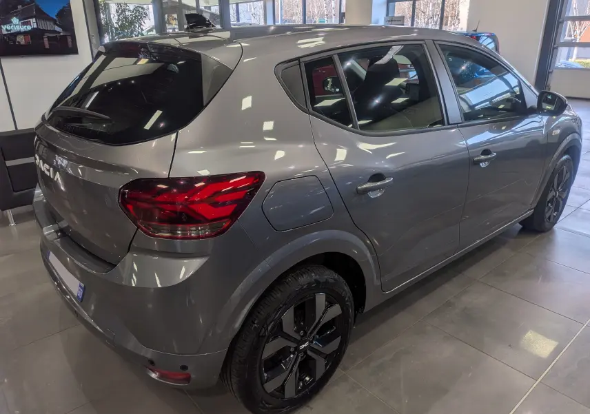 Vue 3/4 arrière droite d'une Dacia Sandero TCe 90 gris schiste avec jantes noires et vitres teintées en showroom.