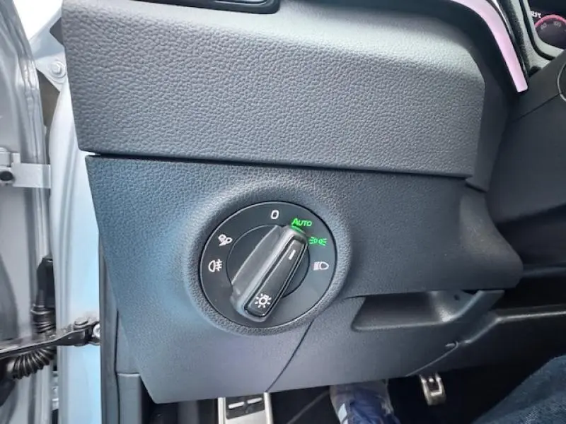 Gros plan sur le bouton de commande des phares côté gauche du tableau de bord gris foncé d’un Skoda Karoq 2025.
