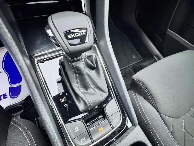 Gros plan sur le levier de vitesses automatique noir avec logo SKODA, entouré de la console centrale intérieure grise.