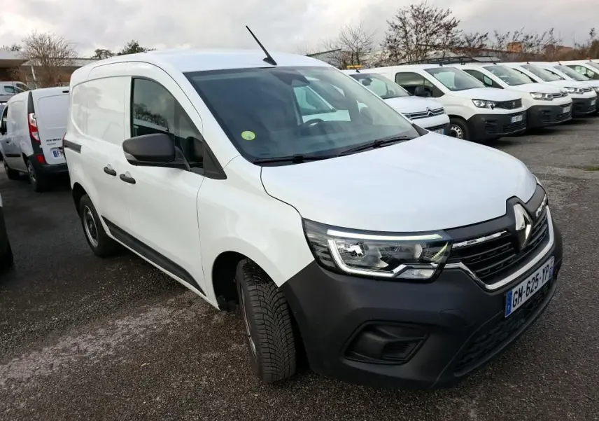 Renault Kangoo blanc en 3/4 avant droit, avec pare-chocs noir et calandre distinctive, stationné en extérieur.