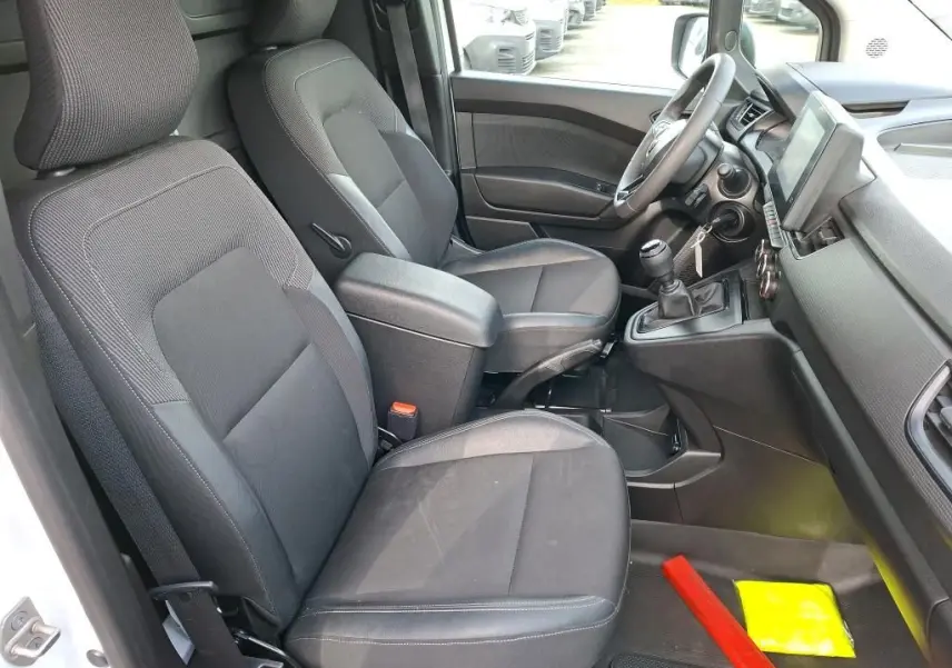 Vue intérieure côté conducteur du Renault Kangoo blanc 2023, montrant les sièges noirs et la console avec boîte manuelle.
