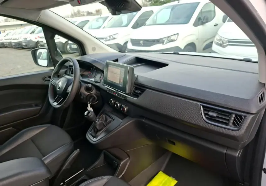 Vue intérieure côté conducteur du Renault Kangoo blanc 2023, mettant en valeur le tableau de bord avec écran tactile et boîte manuelle.