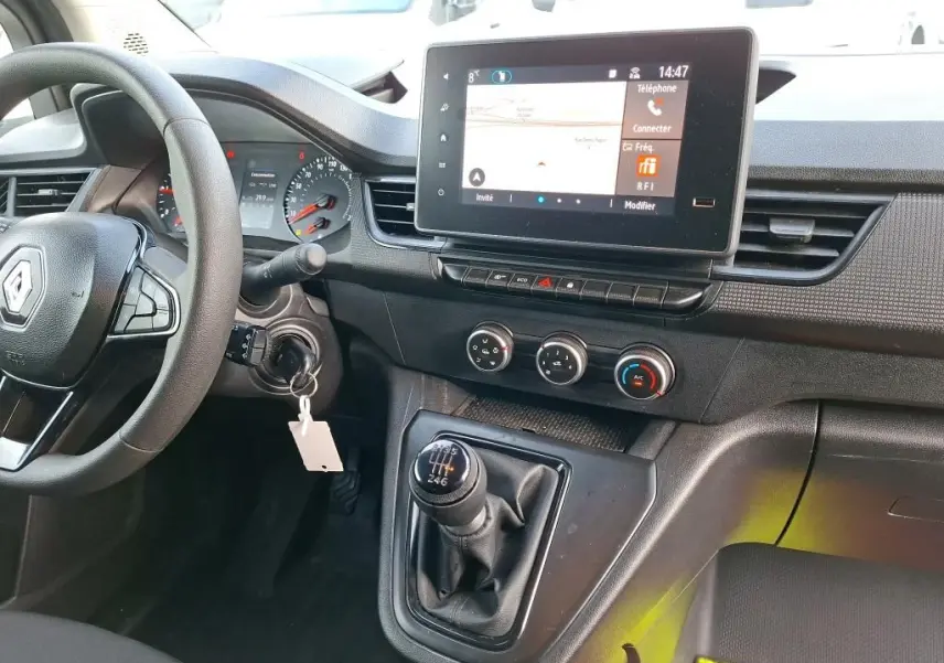 Vue intérieure du tableau de bord et levier de vitesses manuel du Renault Kangoo blanc 2023 avec écran tactile et commandes climatisation.