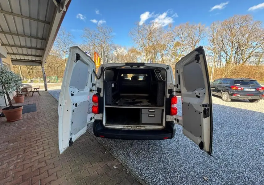 Vue arrière du Peugeot Expert Fourgon blanc 2018 avec portes ouvertes montrant l'intérieur aménagé de rangement.