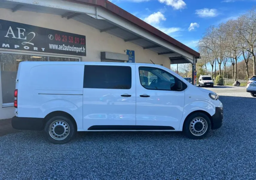 Vue de profil côté gauche du Peugeot Expert Fourgon blanc, version Long 2018, stationné devant un bâtiment.