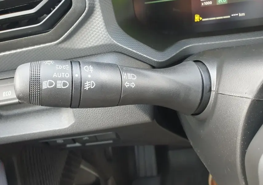 Gros plan sur la commande des feux à gauche du volant dans le tableau de bord du Dacia Duster gris schiste 2026.