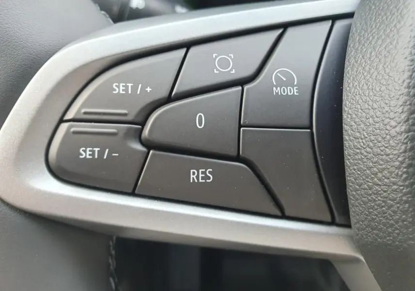 Gros plan sur les commandes noires du volant du Dacia Duster 2026, avec cadre argenté autour des boutons.