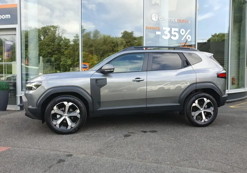 Vue de profil côté gauche d’un Dacia Duster 2026 gris schiste avec jantes alliage 18 pouces et barres de toit.