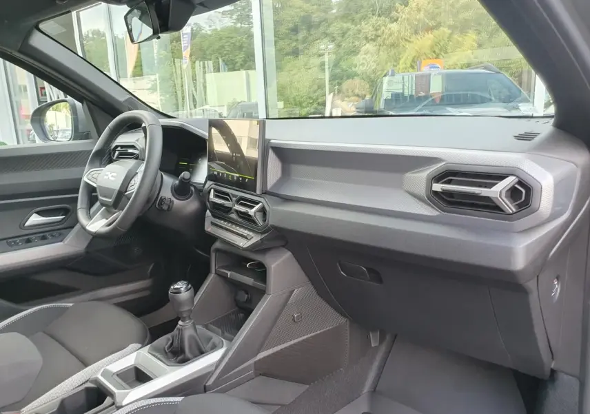 Vue intérieure côté passager du tableau de bord gris et console centrale avec écran tactile du Dacia Duster 2026.