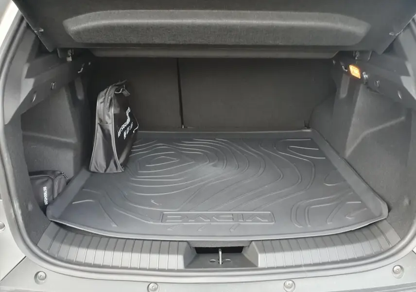 Coffre ouvert du Dacia Duster gris schiste 2026, vue intérieure montrant tapis de coffre et sac de secours noir.