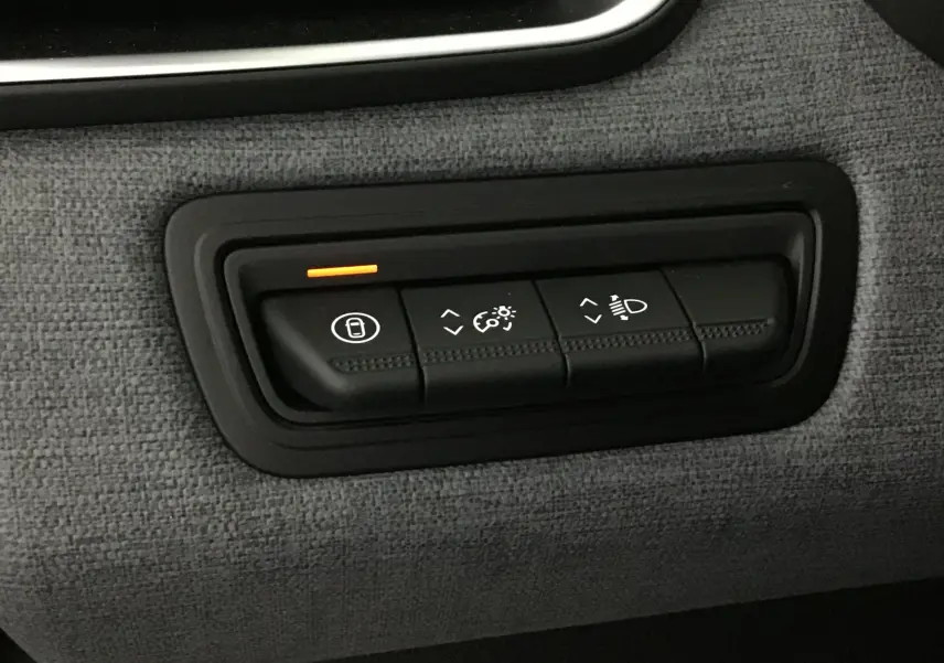 Gros plan sur les commandes d'éclairage et verrouillage de la Renault Clio V 2025, tissu gris schiste en arrière-plan.