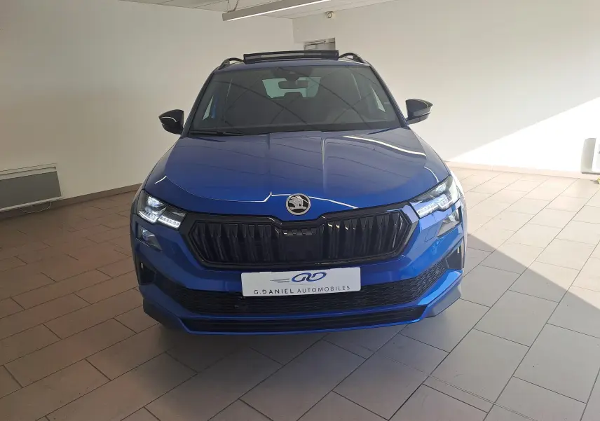 Vue frontale d'un SKODA KAROQ 2025 Bleu RS avec calandre noire et phares LED allumés en intérieur.