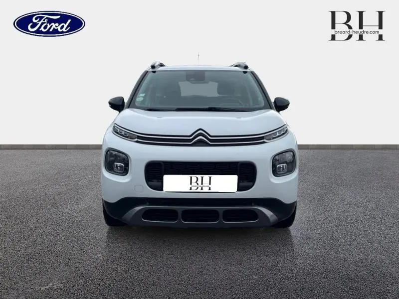 Vue avant d'un Citroën C3 Aircross blanc Natural White avec calandre noire et barres de toit visibles.