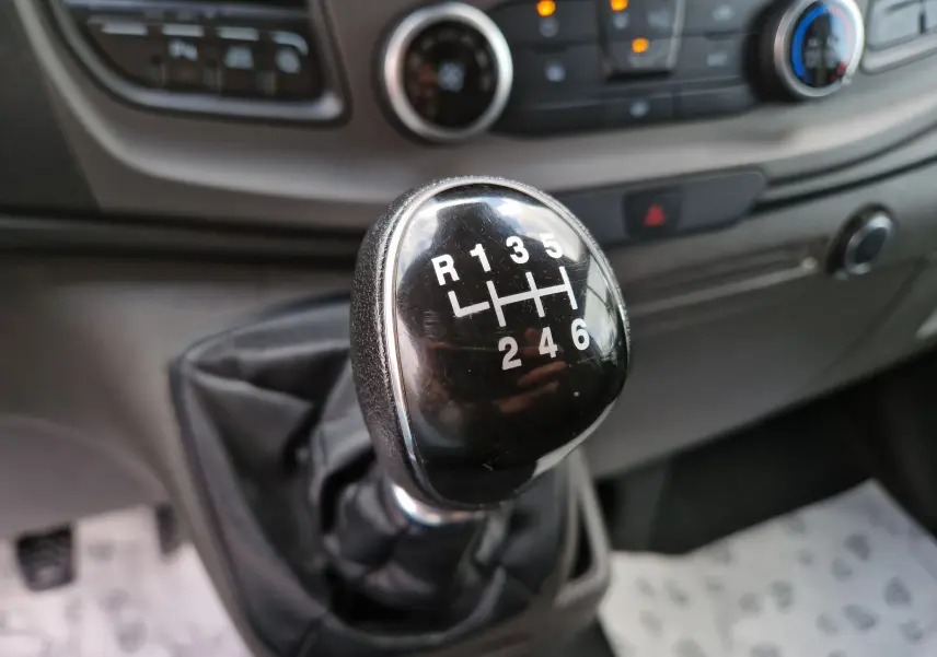 Gros plan sur le levier de vitesses manuel noir du Ford Transit Custom Fourgon blanc, avec tableau de bord en arrière-plan.