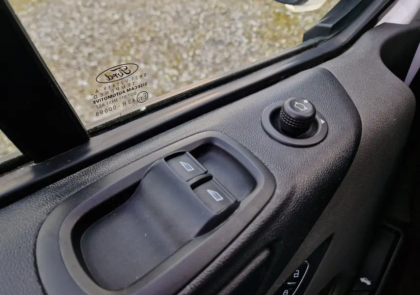 Gros plan sur la commande des vitres et réglage des rétroviseurs côté conducteur du Ford Transit Custom blanc, 2021.