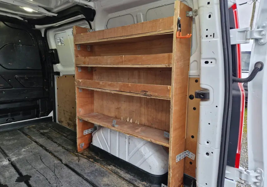 Vue de profil côté gauche d'un Ford Transit Custom blanc avec porte latérale coulissante ouverte révélant l'intérieur aménagé en bois.