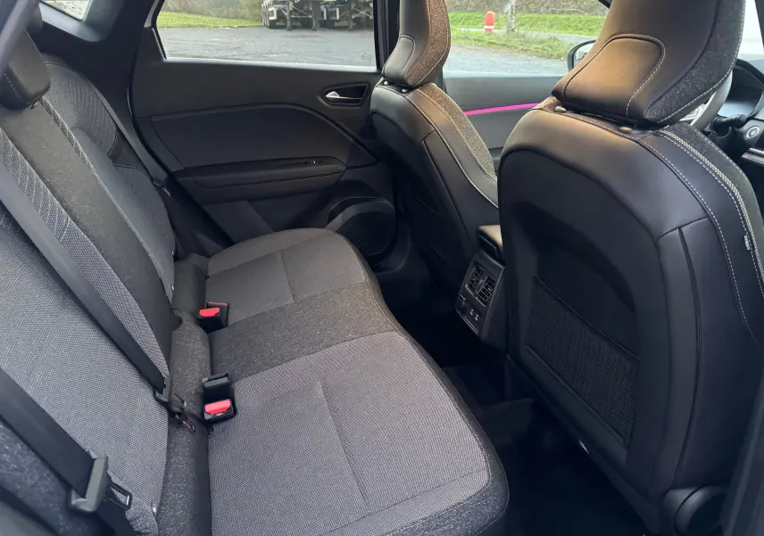 Vue intérieure arrière du Renault Captur E-Tech 2025, sièges tissu gris et dossier avant en cuir noir avec surpiqûres blanches.