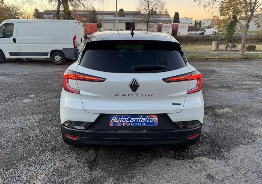 Vue arrière d'un Renault Captur blanc nacré avec toit noir, feux LED allumés, sur un parking extérieur.
