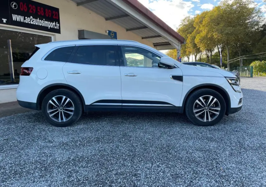 Renault Koleos blanc vu de profil côté gauche, avec jantes alliage et vitres teintées sur parking extérieur.