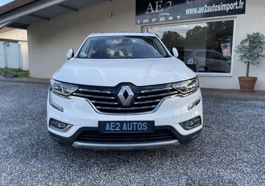 Vue frontale d’un Renault Koleos blanc 2019 avec calandre chromée et phares LED, stationné devant un garage AE2 Autos.