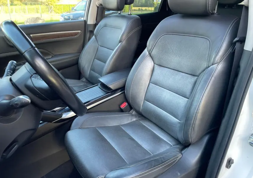 Vue intérieure côté conducteur du Renault Koleos blanc 2019, sièges cuir noirs avec accoudoir central visible.