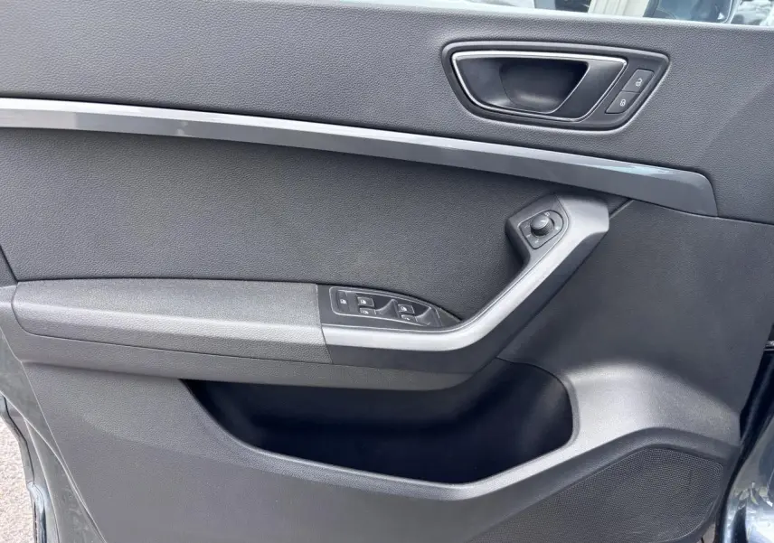 Vue intérieure côté gauche de la porte avant d'une SEAT Ateca gris foncé avec commandes électriques et poignée intégrée.