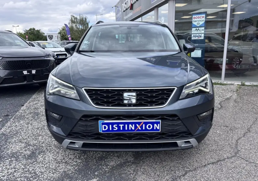 Vue de face d'un SEAT Ateca gris foncé avec calandre noire chromée et phares LED, stationné devant un garage.