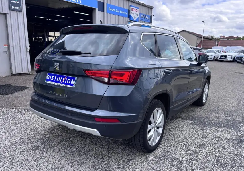 Vue 3/4 arrière droite d’un SEAT Ateca gris foncé avec feux LED et jantes alliage 17 pouces, stationné devant un atelier.