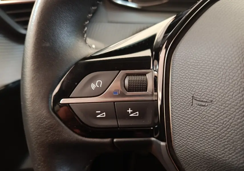 Gros plan sur le volant cuir noir de la Peugeot 208 PureTech 100, avec commandes multifonctions visibles.