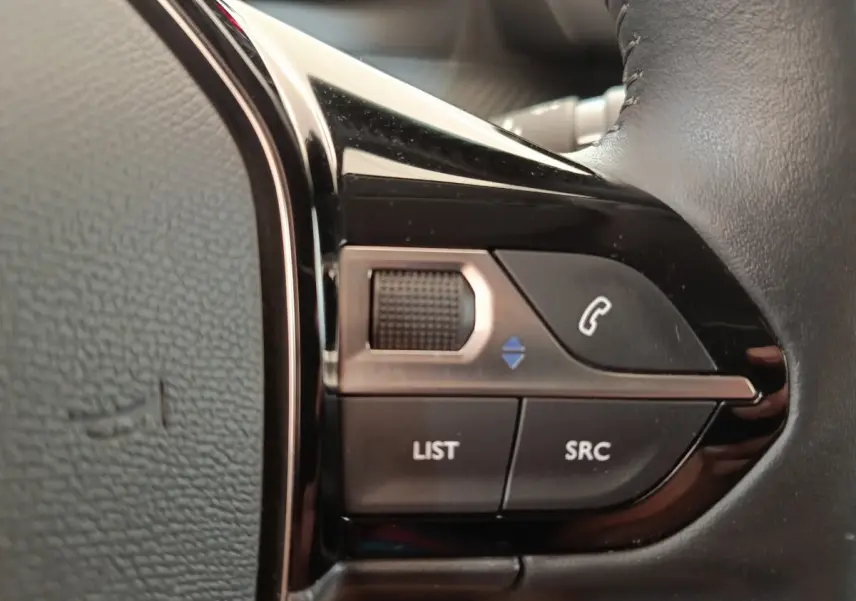 Gros plan sur les commandes noires du volant cuir multifonctions côté gauche d’une Peugeot 208 PureTech 100 S&S Style 2022.