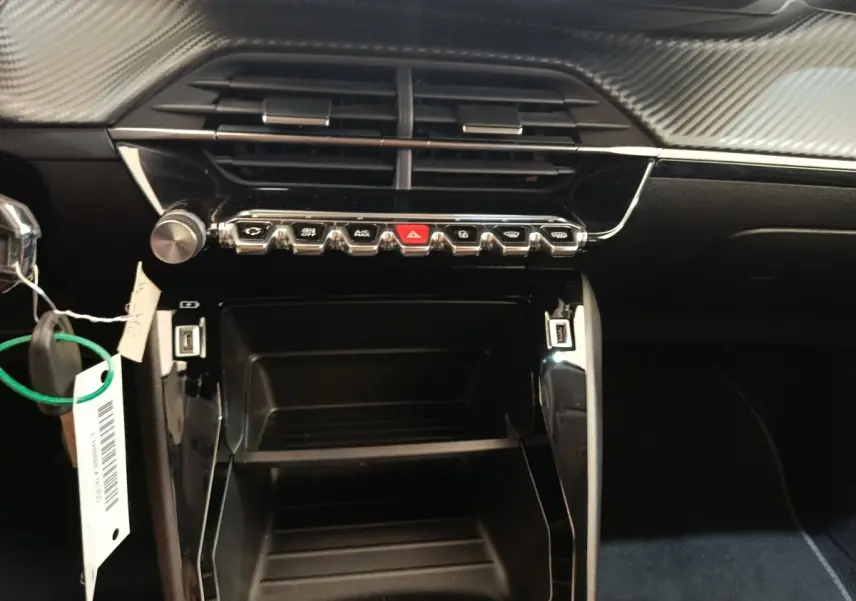 Vue rapprochée du tableau de bord noir de la Peugeot 208 PureTech 100, avec commandes et ports USB visibles.