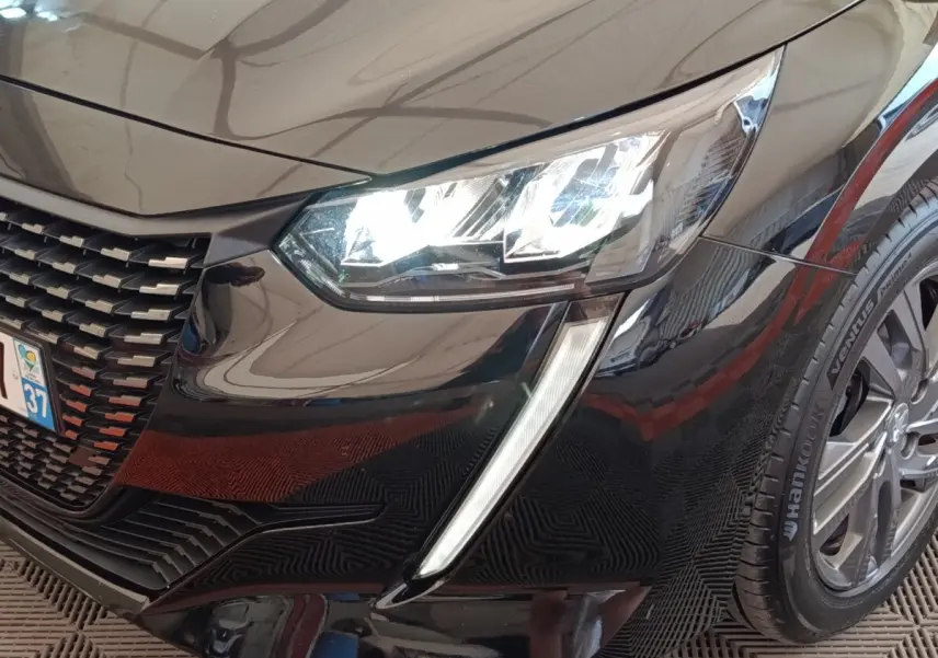 Gros plan sur l'avant droit noir brillant d'une Peugeot 208 2022, mettant en valeur le phare LED et la calandre distinctive.