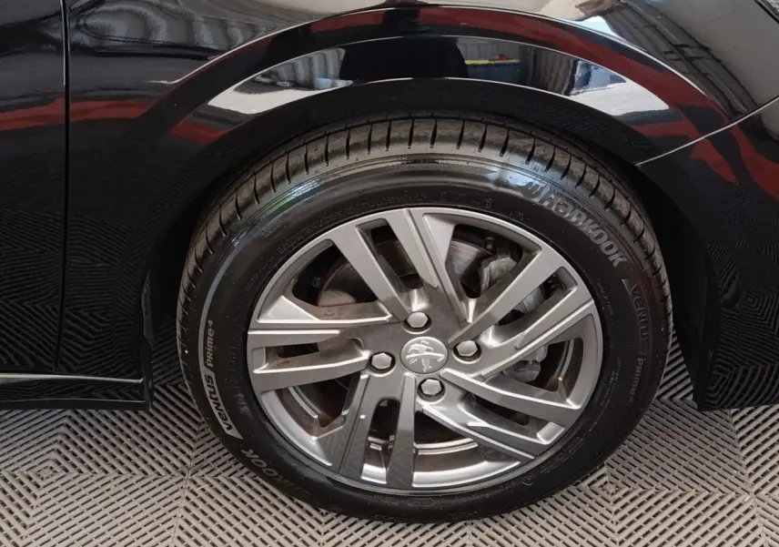 Gros plan sur la roue arrière droite d’une Peugeot 208 noire, jante alliage et pneu Hankook visibles.