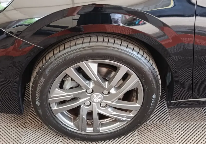 Gros plan sur la roue arrière droite d'une Peugeot 208 noire 2022 avec jante alliage et logo Peugeot visible.