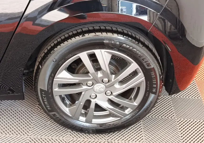 Gros plan sur la roue arrière droite d'une Peugeot 208 noire, mettant en valeur la jante alliage et le pneu Michelin.
