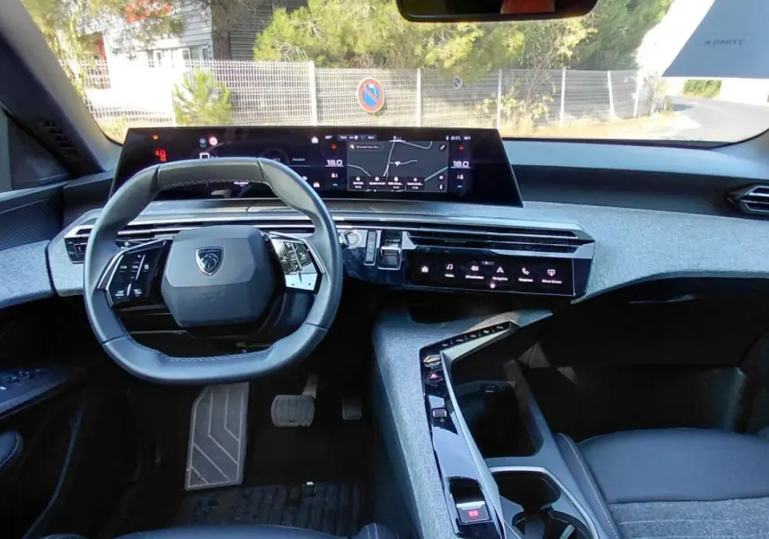 Intérieur du Peugeot 5008 Hybrid 2025 vu de face, tableau de bord moderne avec écran large et volant compact gris.