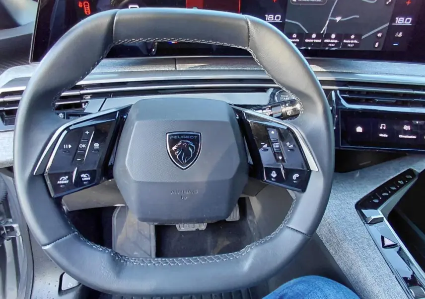 Vue rapprochée du volant cuir noir du Peugeot 5008 Hybrid 2025 avec tableau de bord numérique et commandes tactiles.