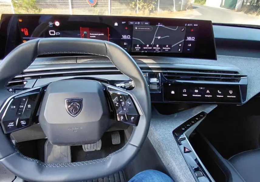 Vue intérieure du poste de conduite du Peugeot 5008 Hybrid gris 2025, avec volant compact et double écran numérique.