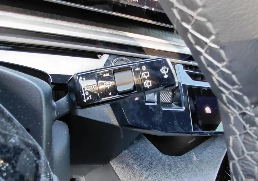 Gros plan sur la commande des essuie-glaces à gauche du volant en cuir gris du Peugeot 5008 Hybrid 2025.