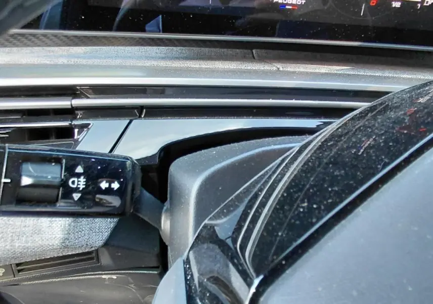 Détail intérieur du Peugeot 5008 Hybrid 2025 montrant la commande des feux et une partie du tableau de bord noir brillant.