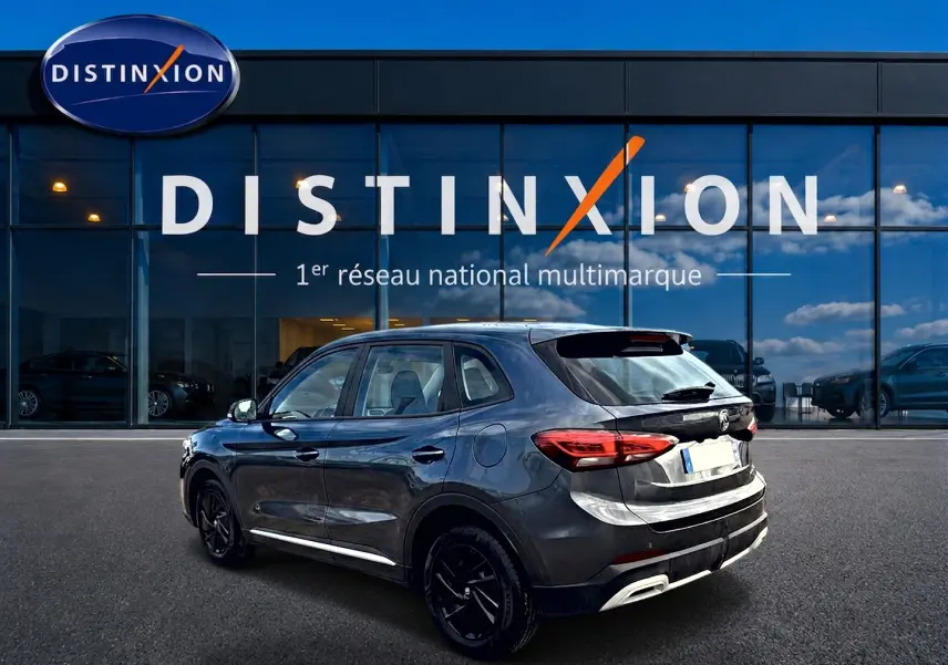 Vue 3/4 arrière droite du MG ZS Camden grey 2026 avec feux LED et jantes noires devant un showroom Distinxion.