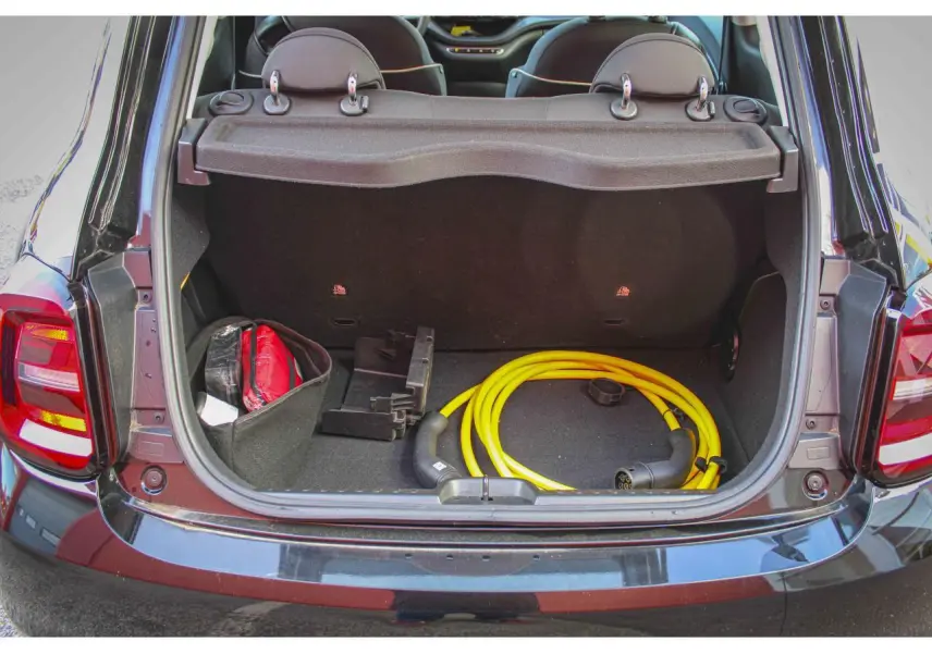 Coffre ouvert vu de l'arrière d'une Fiat 500 électrique noire avec câble de recharge jaune et accessoires rangés.